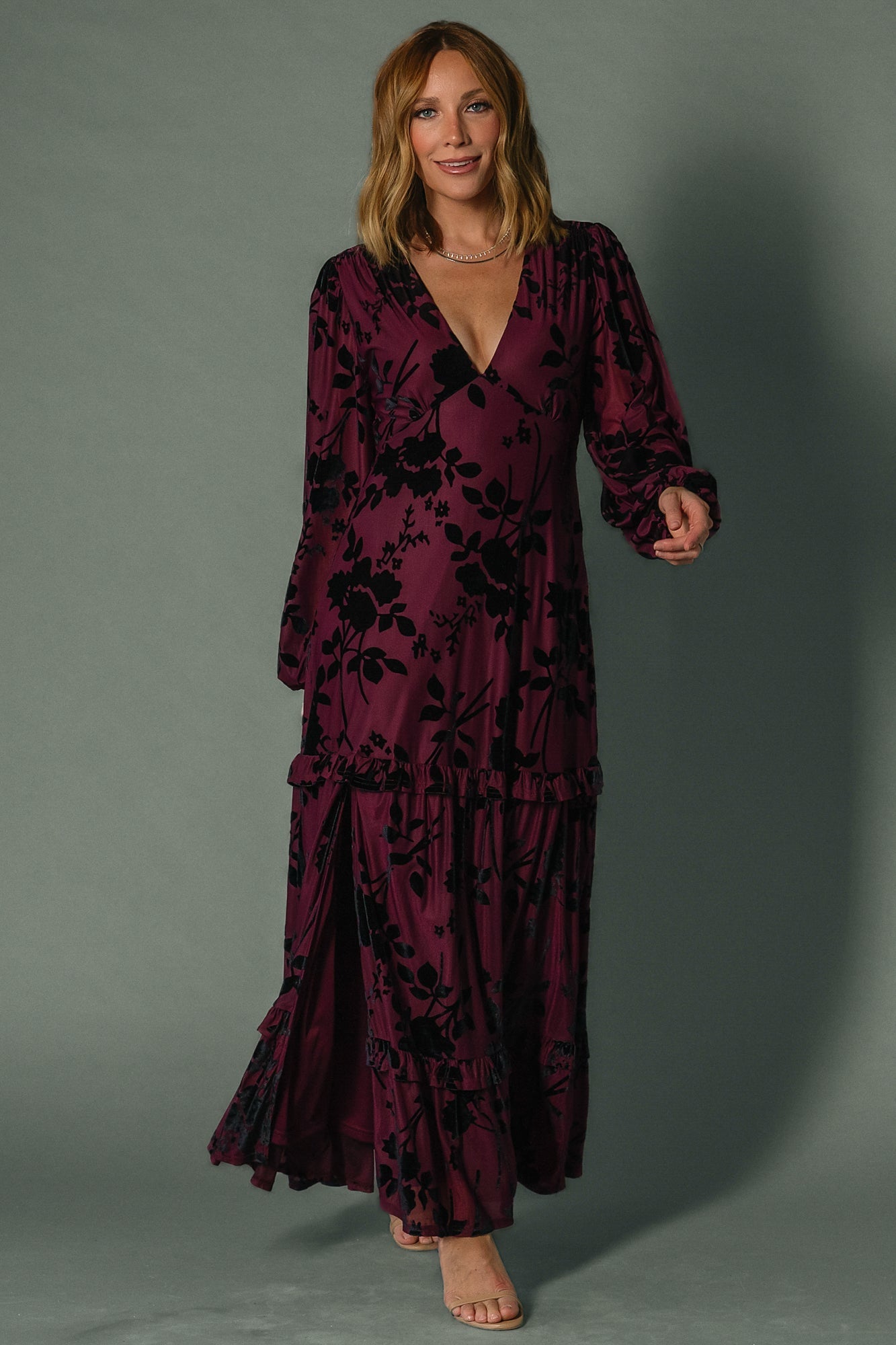 Model wearing mulberry velvet burnout embossed maxi dress, long sleeves, plunging V-neck, ruffle tiered skirt flowing to ankles.