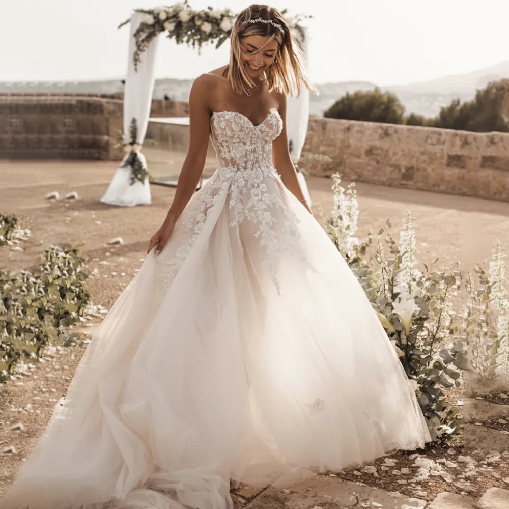 Bride wearing a boho lace wedding dress featuring crystal lace appliqués, sweetheart neckline, off-the-shoulder sleeves, flowing A-line skirt, lace-up corset back, and elegant court train for a romantic outdoor wedding.